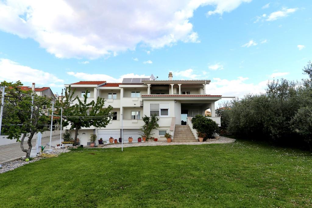 une grande maison blanche avec une cour en herbe dans l'établissement Villa Mičić, à Zadar