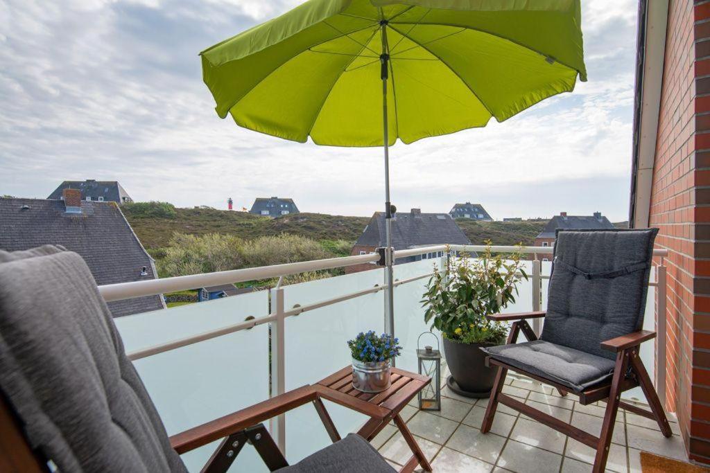 a patio with two chairs and an umbrella on a balcony at Appartement-Leuchtturmblick in Hörnum