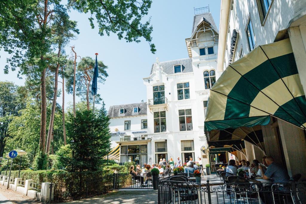 um grupo de pessoas sentadas em mesas em frente a um edifício em Parkhotel Mastbosch Breda em Breda