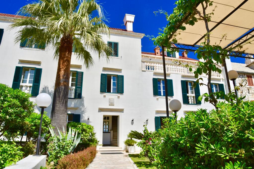 a white house with green shutters and a palm tree at Villa Giardino Heritage Boutique Hotel Bol in Bol