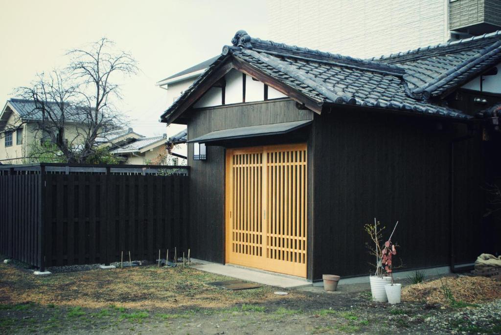 ein schwarzes Haus mit einer Holztür neben einem Zaun in der Unterkunft NARAigoto EENA HOUSE in Nara