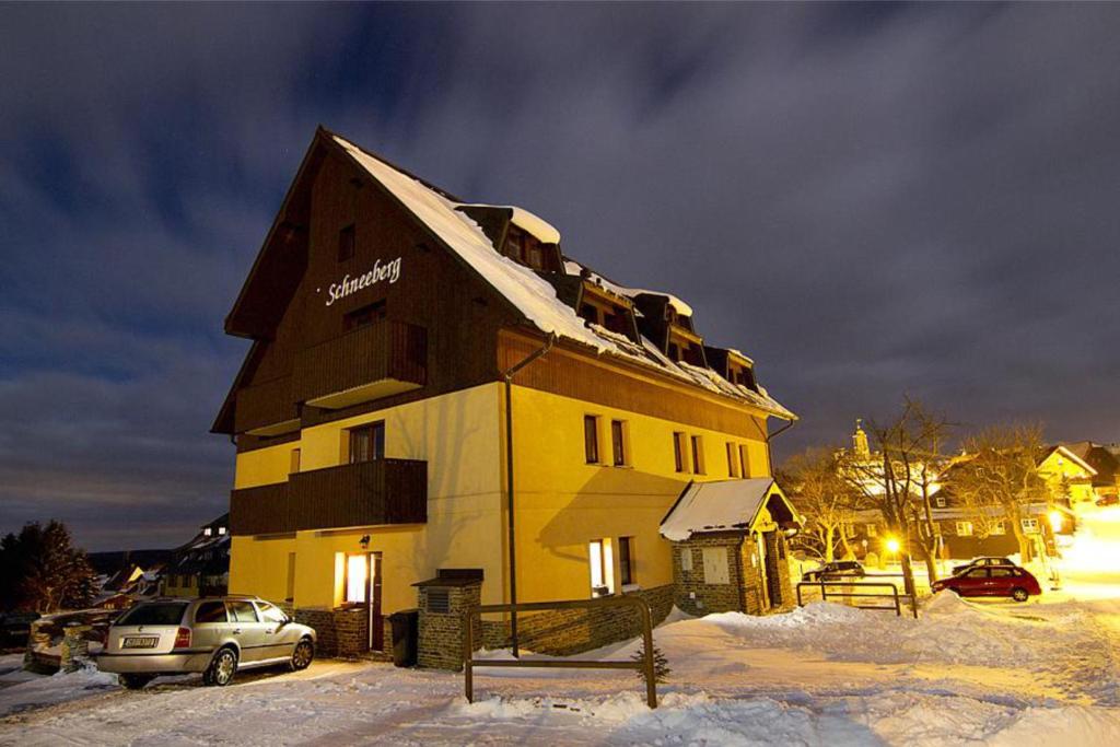 ein großes gelbes Gebäude im Schnee in der Nacht in der Unterkunft Schneeberg Apartmany in Boží Dar