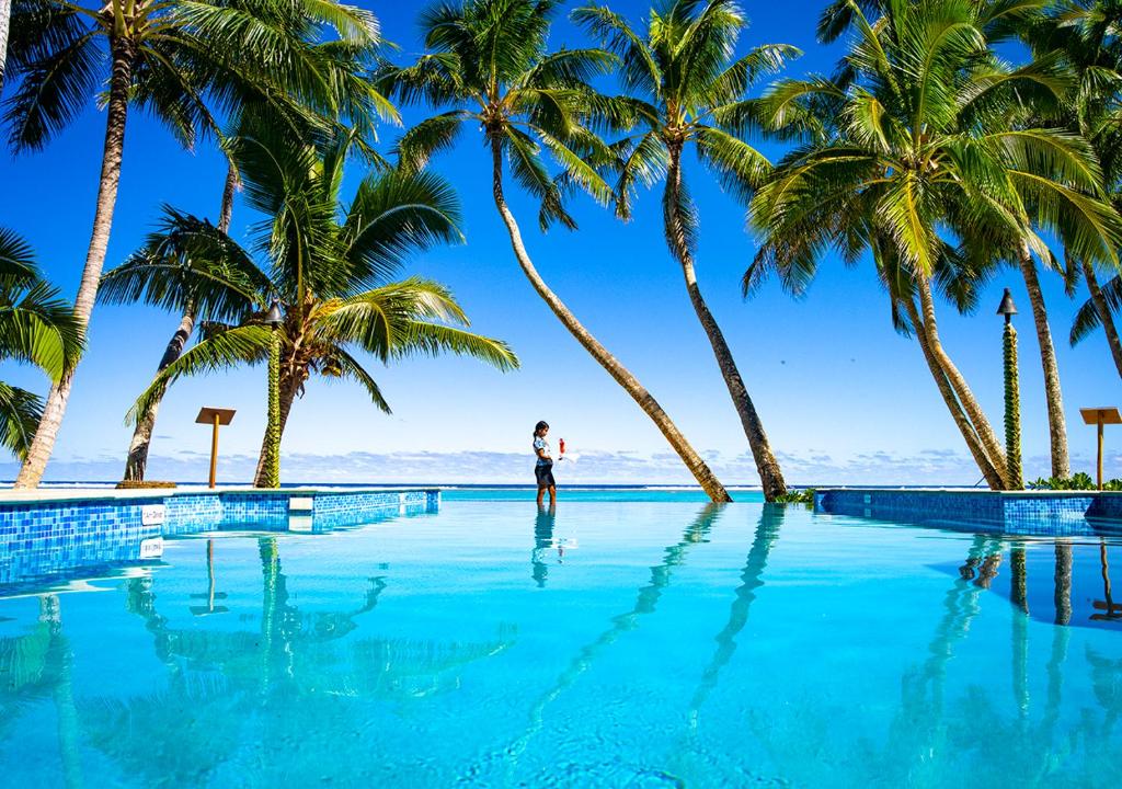 un uomo in piedi di fronte a una piscina con palme di Little Polynesian Resort a Rarotonga