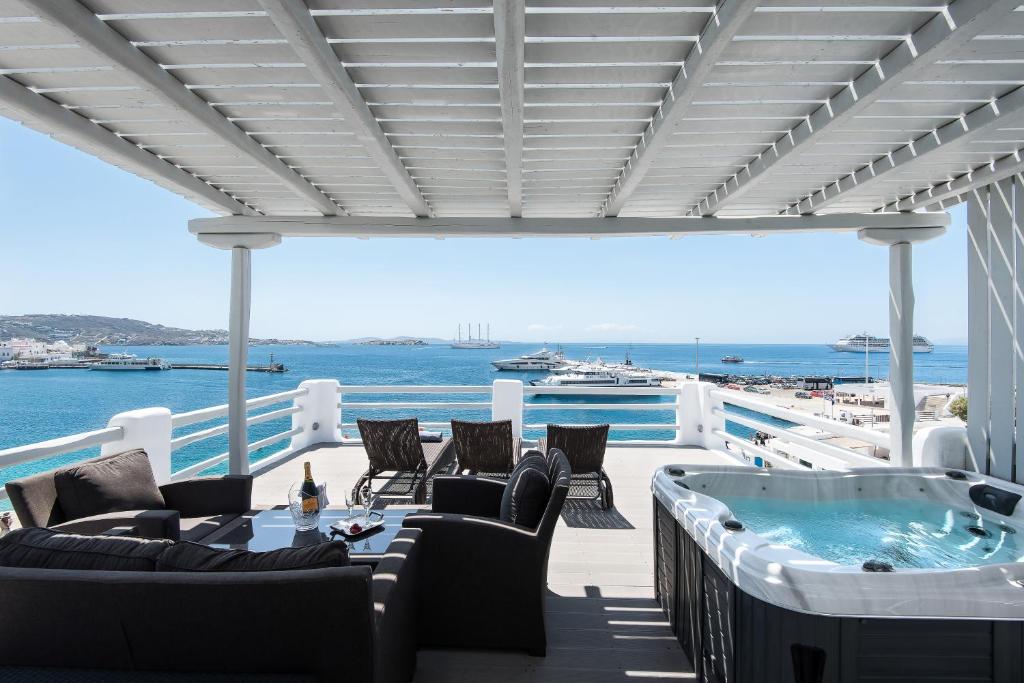 een patio met een hot tub en stoelen en de oceaan bij Riva Suites - Adults Only in Mykonos-stad