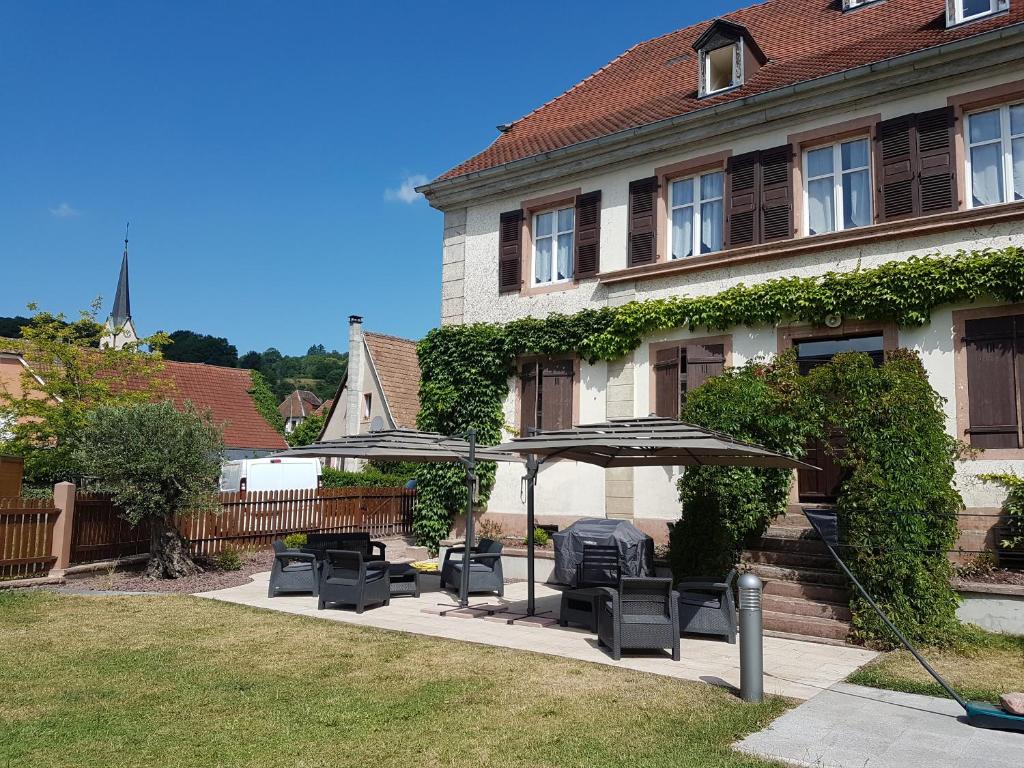 a house with a group of chairs and an umbrella at Ancien Presbytère Albert Schweitzer in Gunsbach