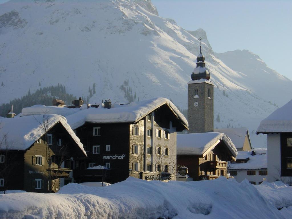 a building with a clock tower and a snow covered mountain at Hotel Sandhof in Lech am Arlberg