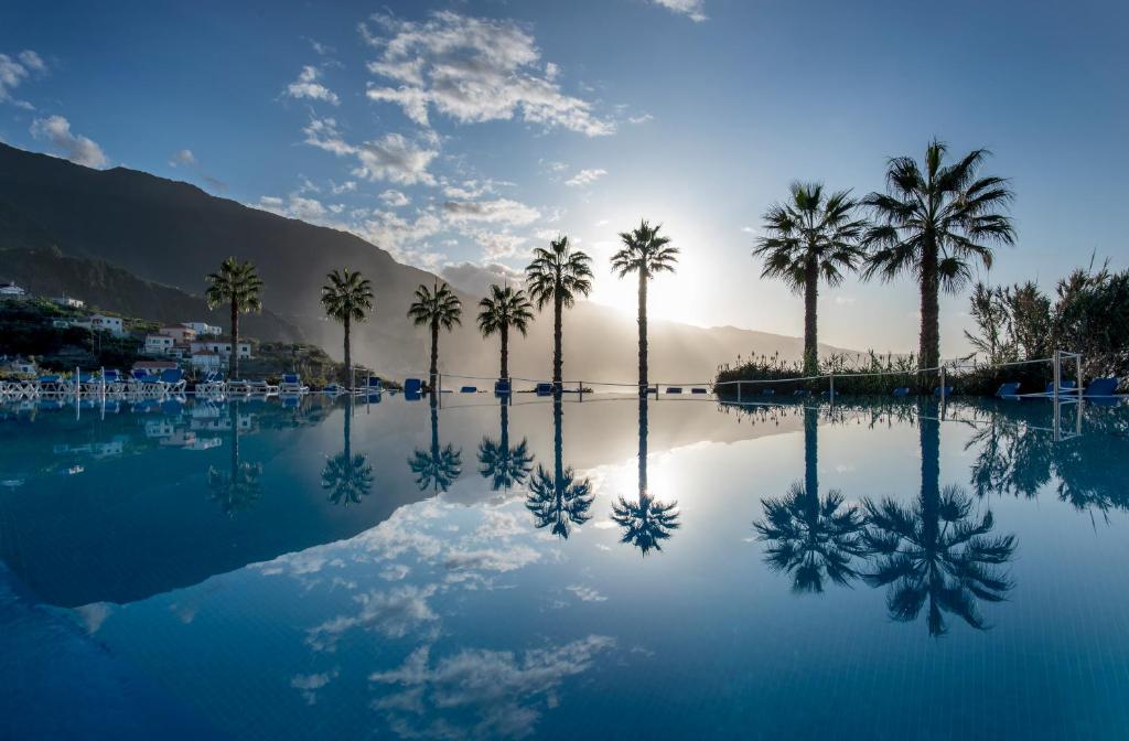 una piscina de agua con palmeras y montañas en Monte Mar Palace Hotel, en Ponta Delgada