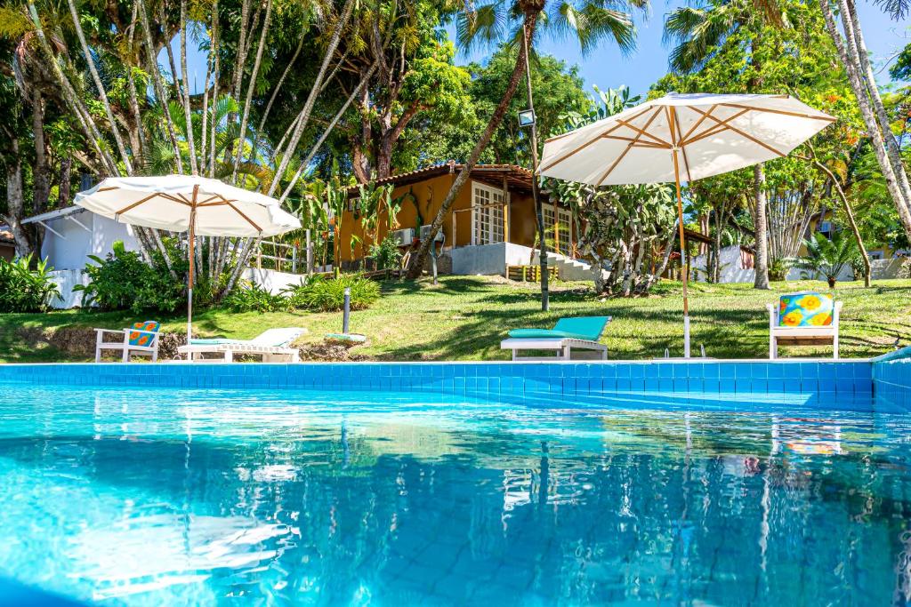 une piscine avec deux parasols et une maison dans l'établissement Pousada Rio da Vila, à Porto Seguro