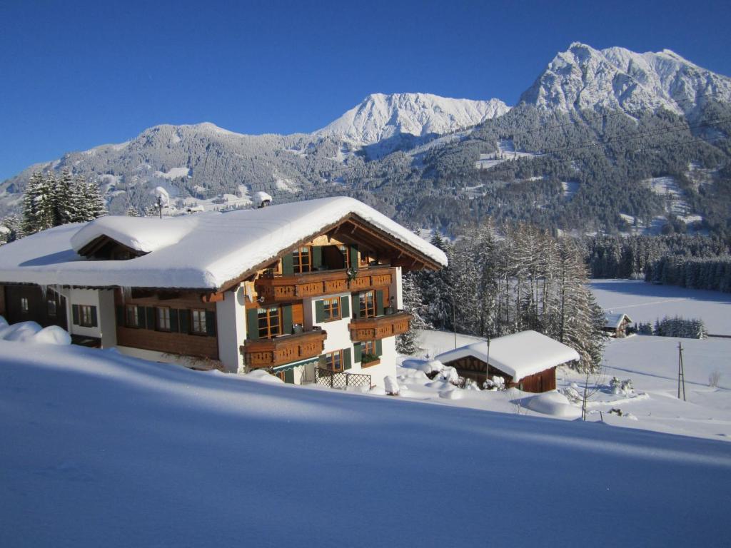 une maison recouverte de neige avec des montagnes en arrière-plan dans l'établissement Landhaus Eggensberger, à Fischen im Allgäu