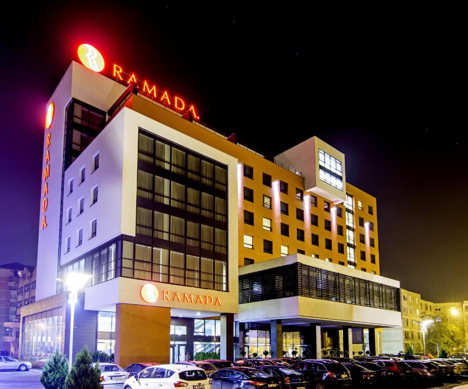 un hôtel avec des voitures garées dans un parking la nuit dans l'établissement Ramada by Wyndham Oradea, à Oradea