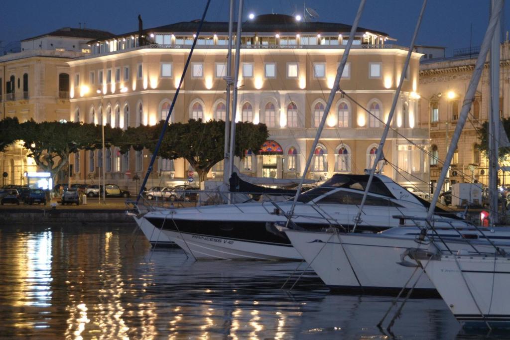 eine Gruppe von Booten im Wasser vor einem Gebäude in der Unterkunft Grand Hotel Ortigia in Syrakus