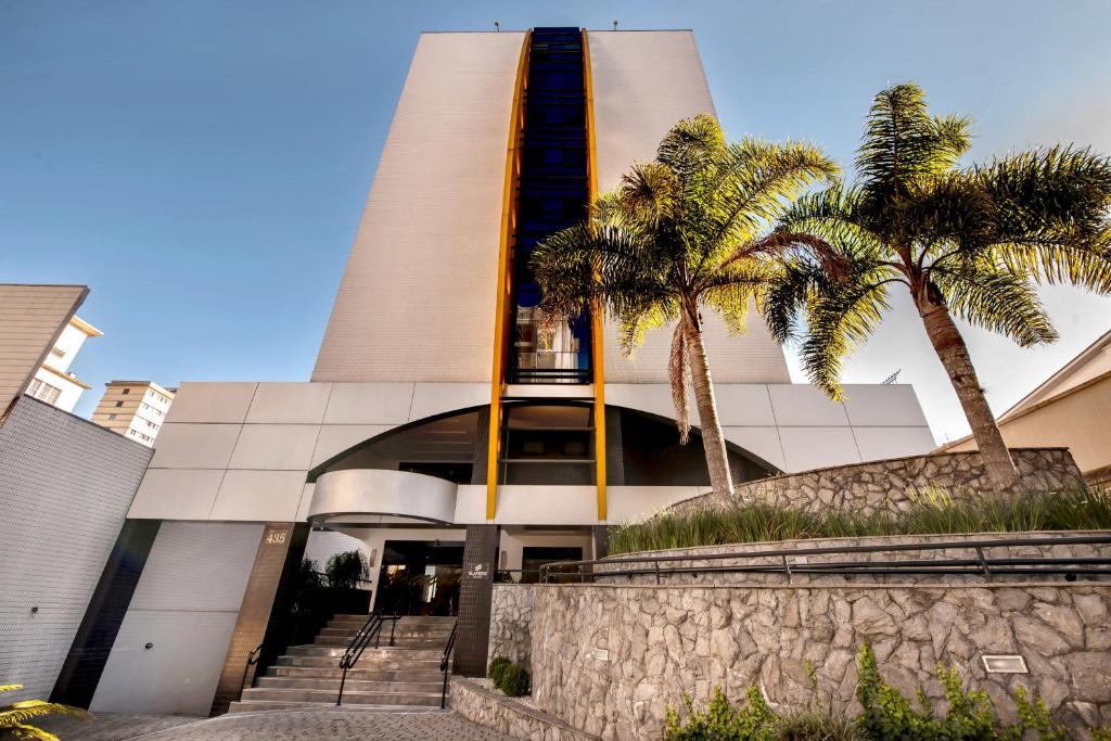 un edificio con palmeras delante en Slim Curitiba Alto da XV, en Curitiba