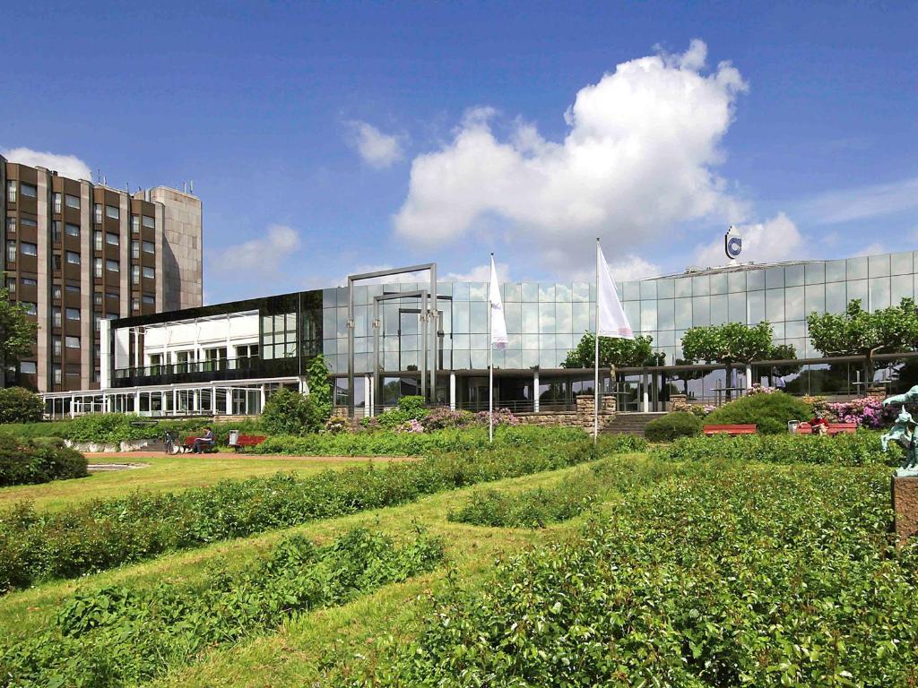 un grand bâtiment en verre avec deux drapeaux blancs devant lui dans l'établissement Mercure Hotel Dortmund Messe, à Dortmund