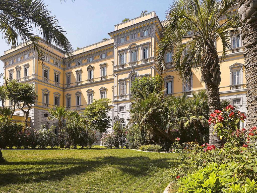 ein großes gelbes Gebäude mit Palmen davor in der Unterkunft GH Palazzo Suite & SPA in Livorno