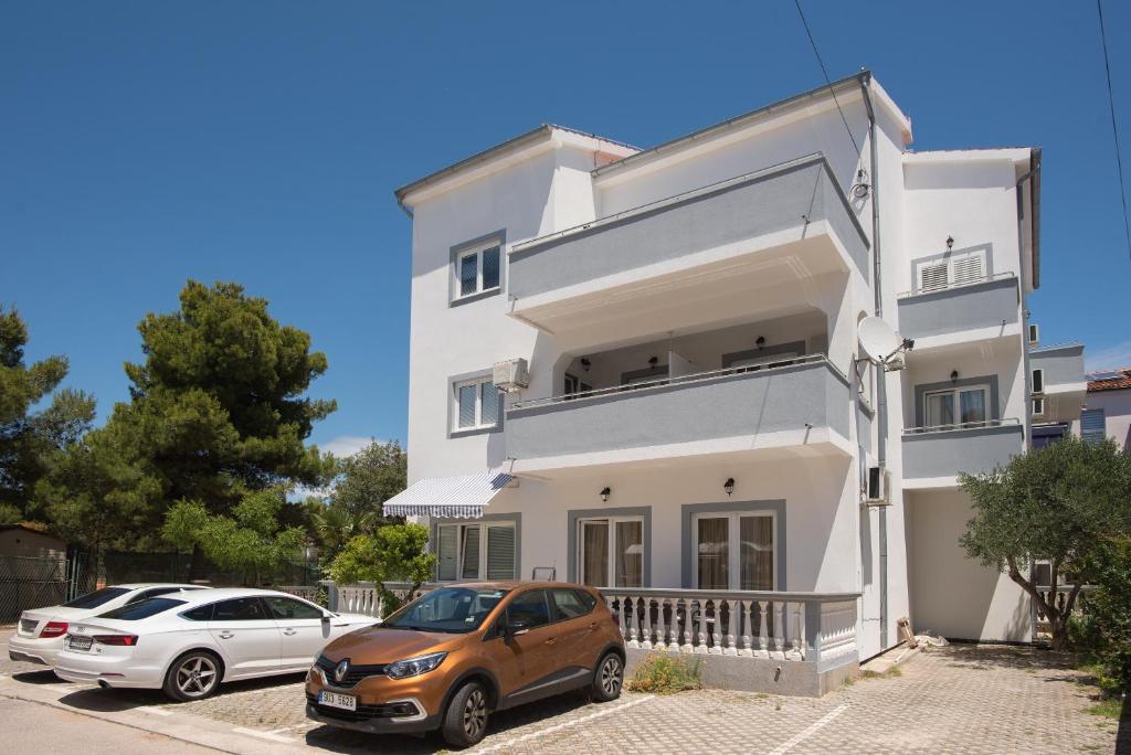 ein weißes Haus mit zwei Autos davor geparkt in der Unterkunft Apartments Lovrić in Vodice