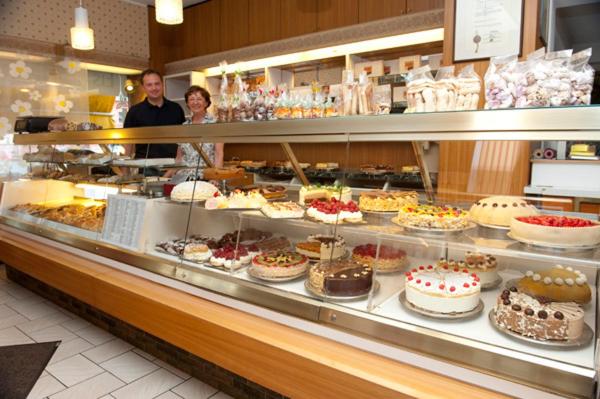 duas pessoas atrás de uma padaria com bolos e doces em Hotel Goldinger em Landstuhl