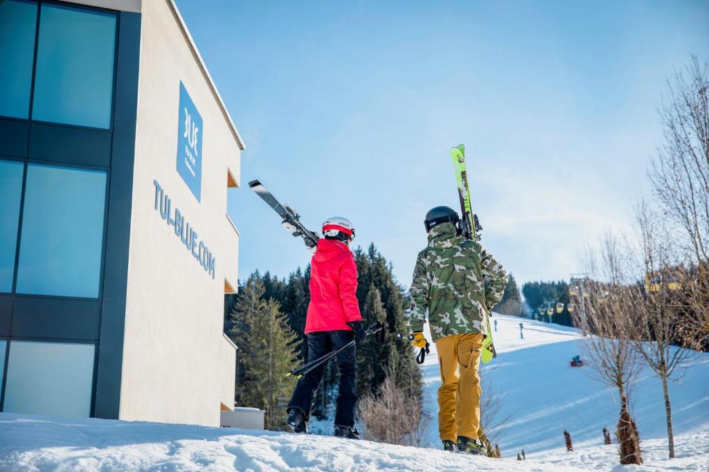 2 personnes tenant leurs skis dans un bâtiment dans l'établissement TUI BLUE Fieberbrunn, à Fieberbrunn