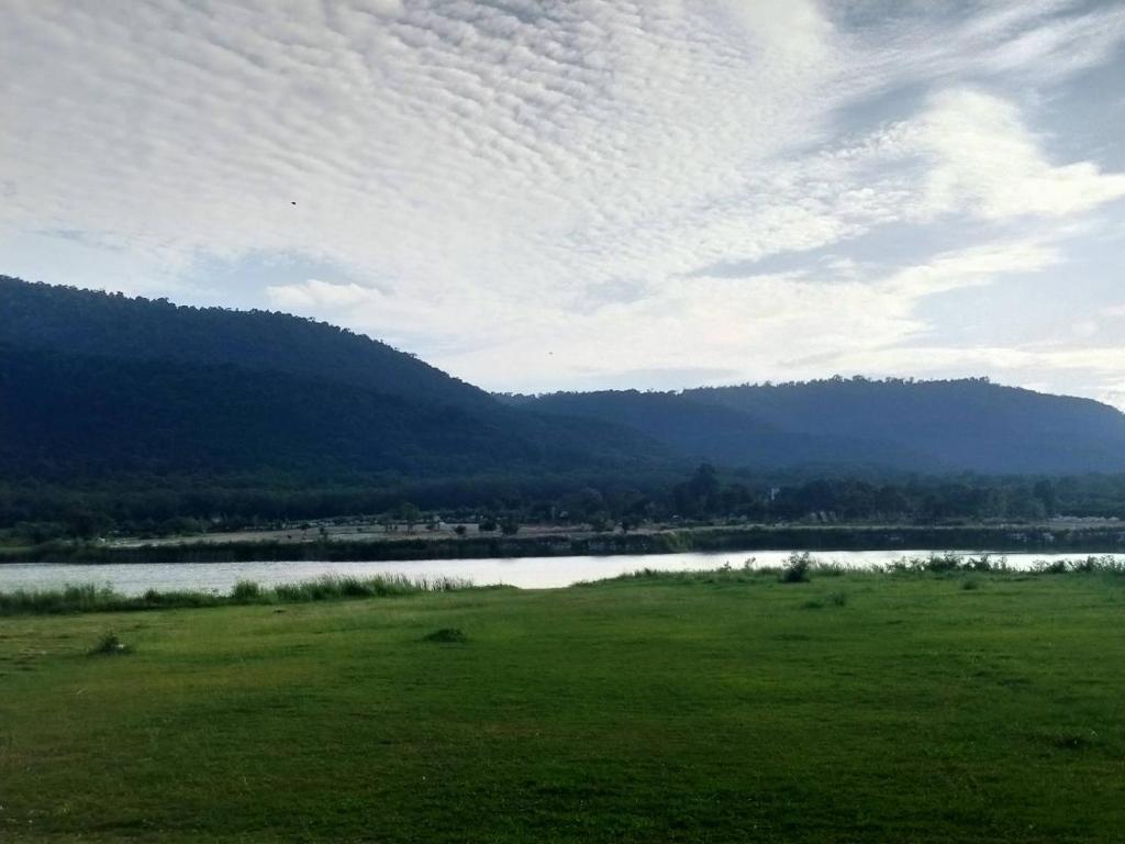 um campo verde com um lago e montanhas ao fundo em Samerdrow Khao Yai em Mu Si