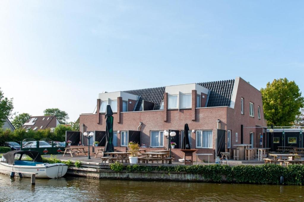 una casa en el agua con mesas y un barco en De Watersport Heeg, en Heeg