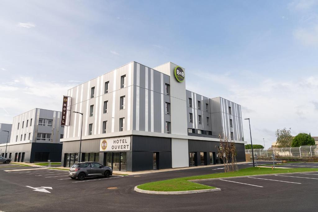 un grande edificio bianco con un'auto parcheggiata in un parcheggio di B&B HOTEL Poitiers Aéroport a Poitiers