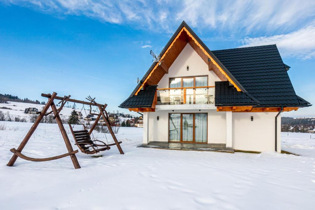 uma casa na neve com um baloiço em Tatra Apartments z zewnętrznym jacuzzi em Biały Dunajec