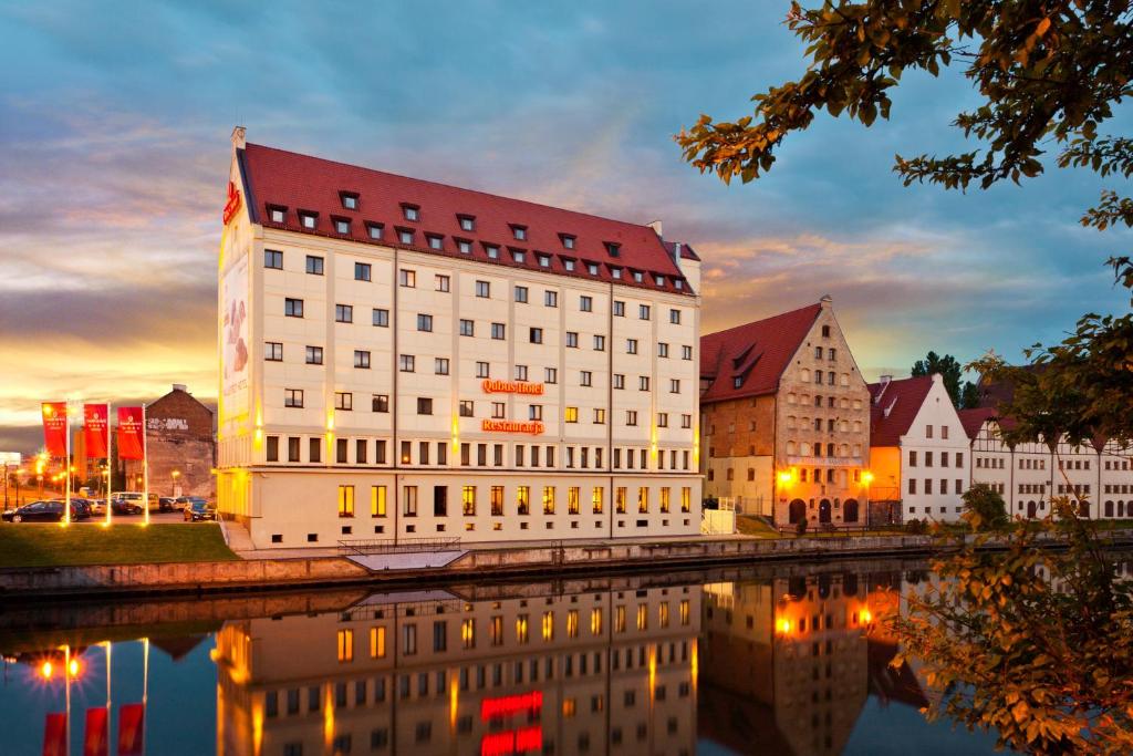 a large white building with a red roof next to a river at Qubus Hotel Gdańsk in Gdańsk