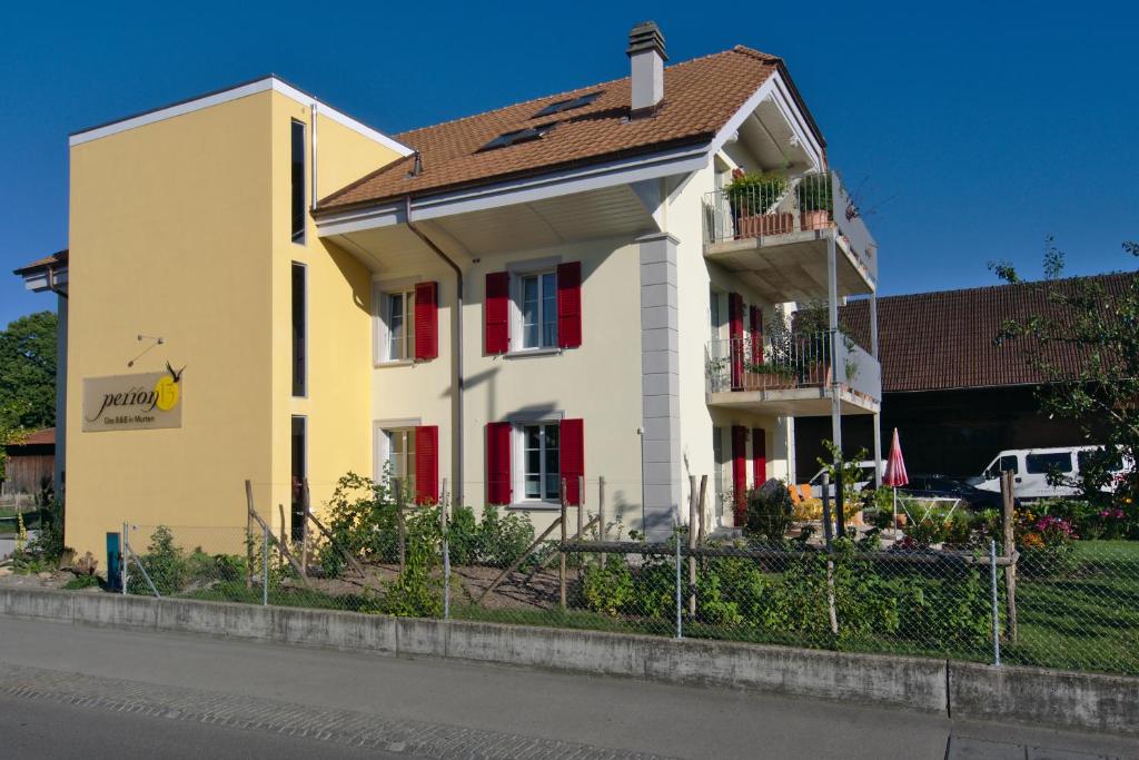 una casa amarilla con ventanas rojas y una valla en B&B Perron13, en Murten