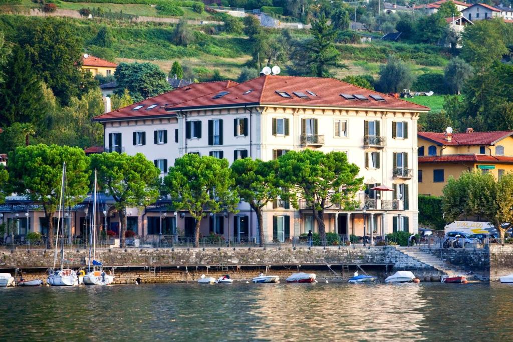 ein großes weißes Gebäude mit rotem Dach auf dem Wasser in der Unterkunft Hotel Lenno in Lenno