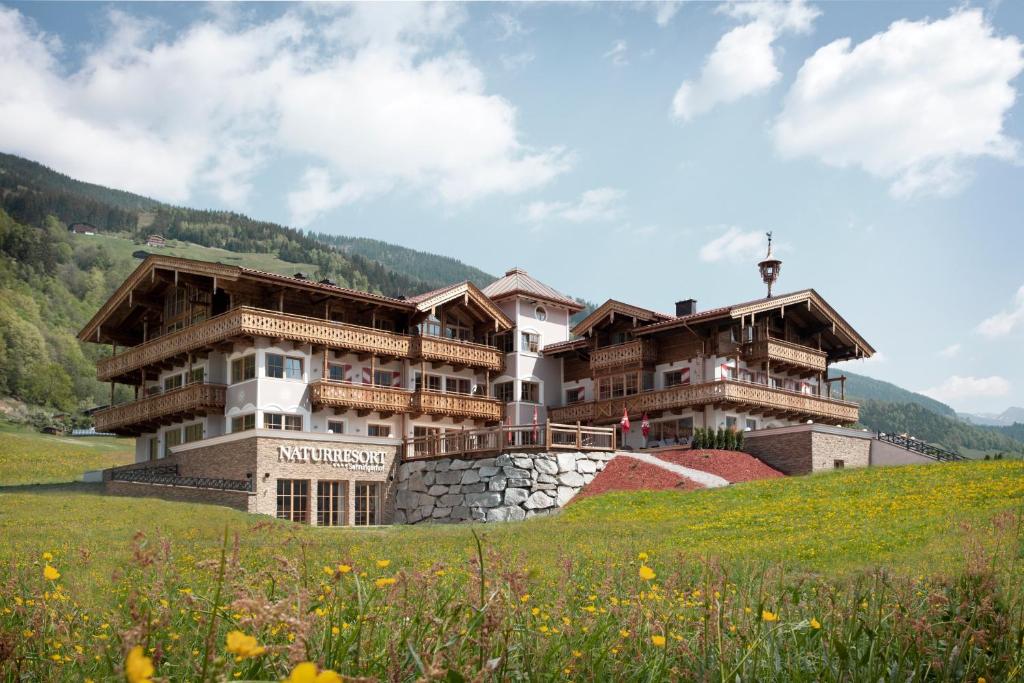 un grand bâtiment sur une colline dans un champ dans l'établissement Naturresort Senningerhof, à Bramberg am Wildkogel