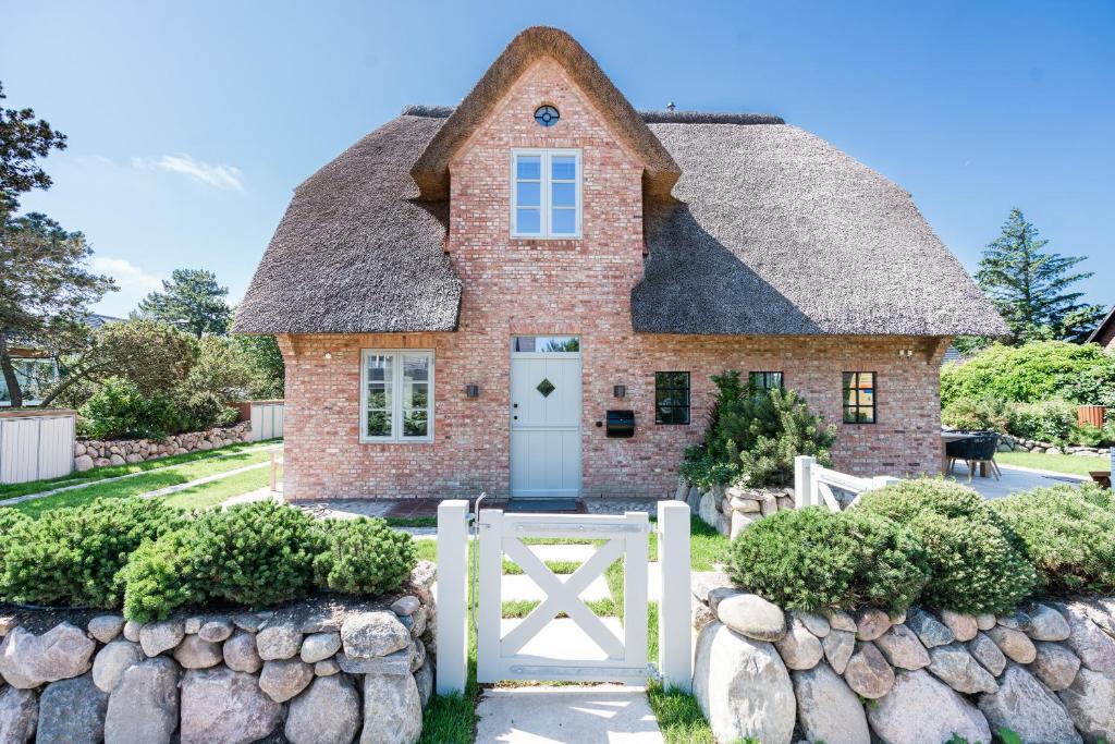 une maison en briques avec un toit de chaume et une clôture blanche dans l'établissement Loddis Hüs, à Wenningstedt