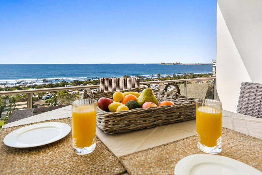 una mesa con una cesta de fruta y dos vasos de zumo de naranja en Silver Sapphire on Sixth Penthouse, en Maroochydore