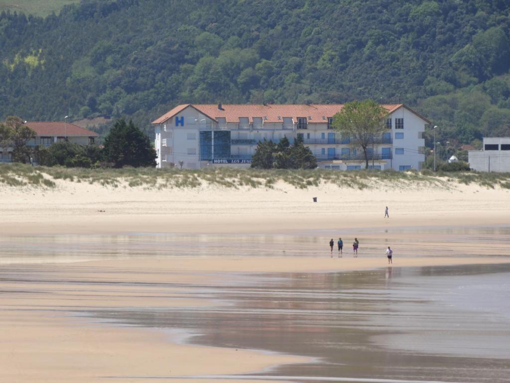 duas pessoas a caminhar numa praia com um edifício ao fundo em Hotel Los Juncos em Noja