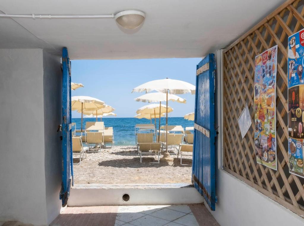 una puerta abierta a la playa con sillas y sombrillas en Hotel Del Sole, en Santa Marinella