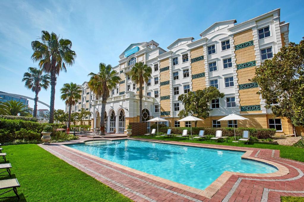 una piscina frente a un edificio con palmeras en StayEasy Century City, en Ciudad del Cabo