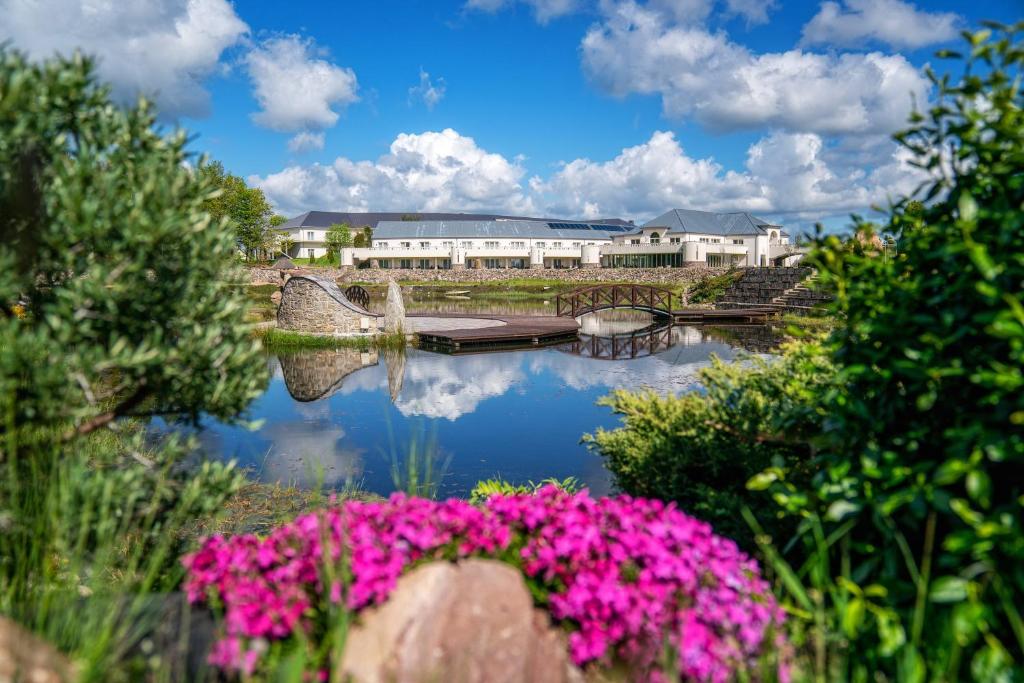 - une vue sur une maison et une rivière avec des fleurs roses dans l'établissement Hotel Kiston, à Sulęczyno