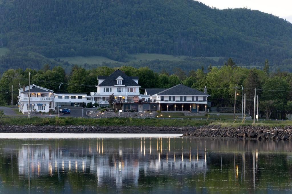 een groot wit huis naast een waterlichaam bij Hôtel Aquamer in Carleton sur Mer