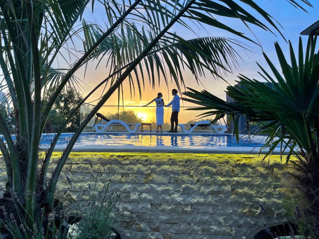 zwei Personen stehen am Rande eines Pools bei Sonnenuntergang in der Unterkunft AM Palace in Ulcinj