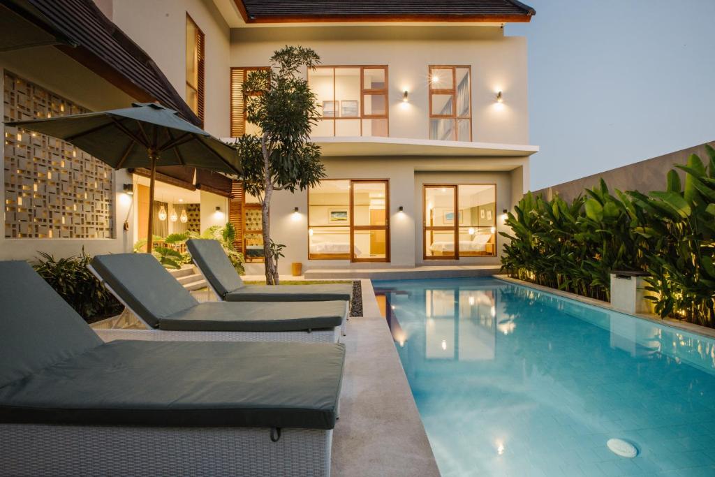 una casa con piscina con sedie e ombrellone di Vasudha Hostel Canggu a Canggu