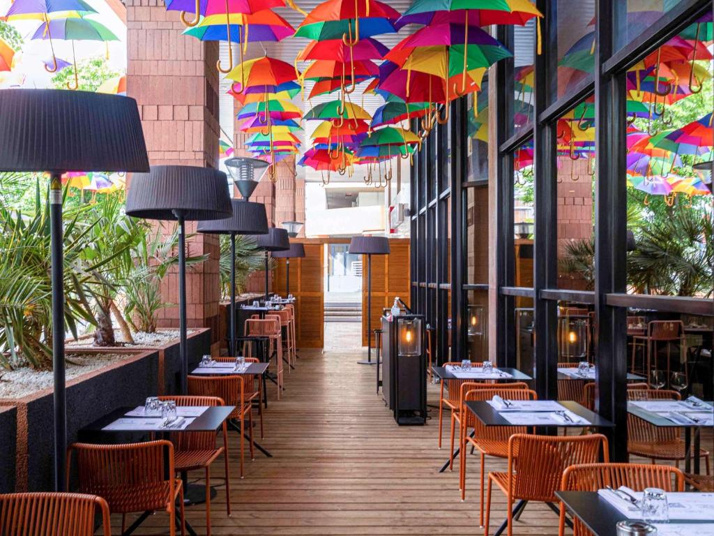 un restaurant avec des tables et des parasols suspendus aux plafonds dans l'établissement Pullman Toulouse Centre Ramblas, à Toulouse