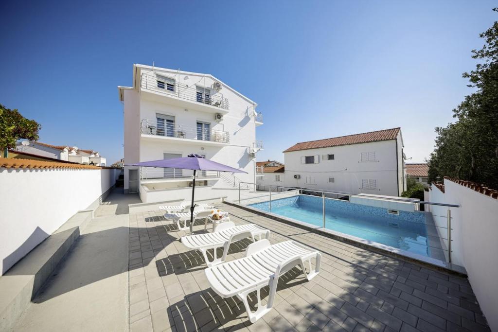 Infinity Appartements in Vodice - Nord-Dalmatien في فوديس: بلكونه مع مسبح وكراسي ومبنى