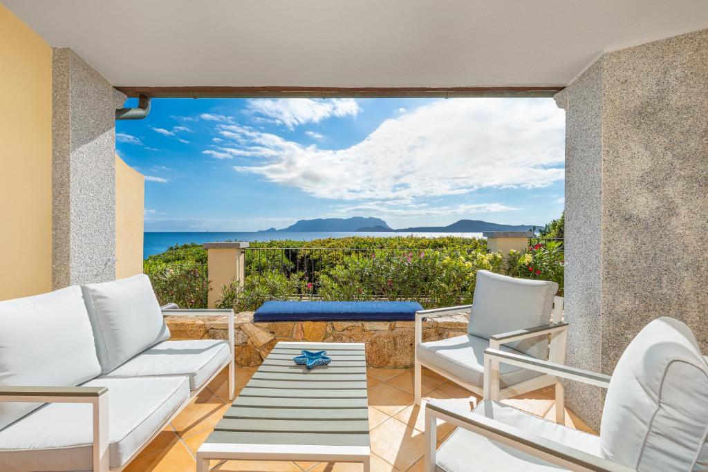 un patio con muebles blancos y vistas al océano. en Terrazza su Tavolara, en Olbia