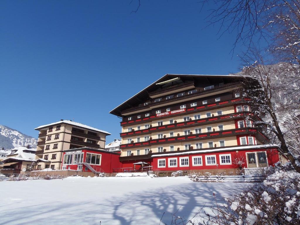 Hotel Germania Gastein - ganzjährig inklusive Alpentherme Gastein & Sommersaison inklusive Gasteiner Bergbahnen في باد هوفغاستين: مبنى احمر كبير مع ثلج أمامه