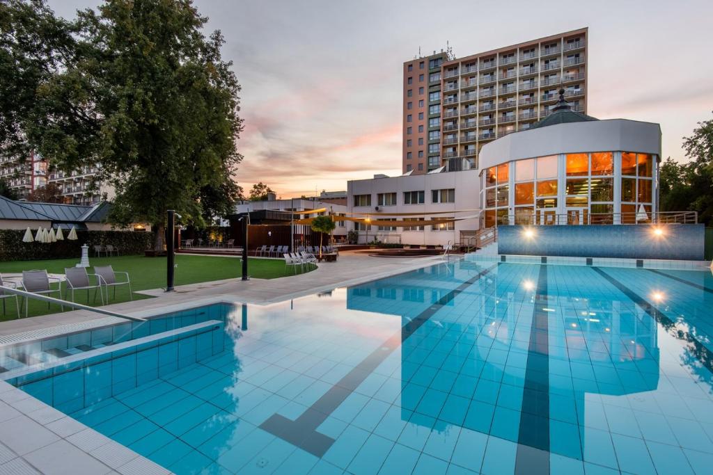 uma piscina de hotel com um edifício ao fundo em Hotel Barátság em Hajdúszoboszló