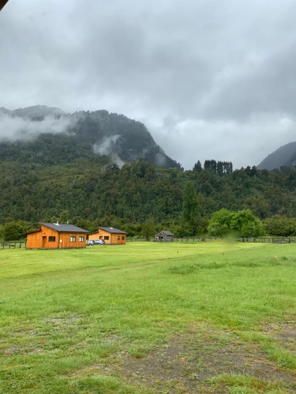 un campo verde con una casa y una montaña en Cabañas Río del Este SPA, en Puerto Varas