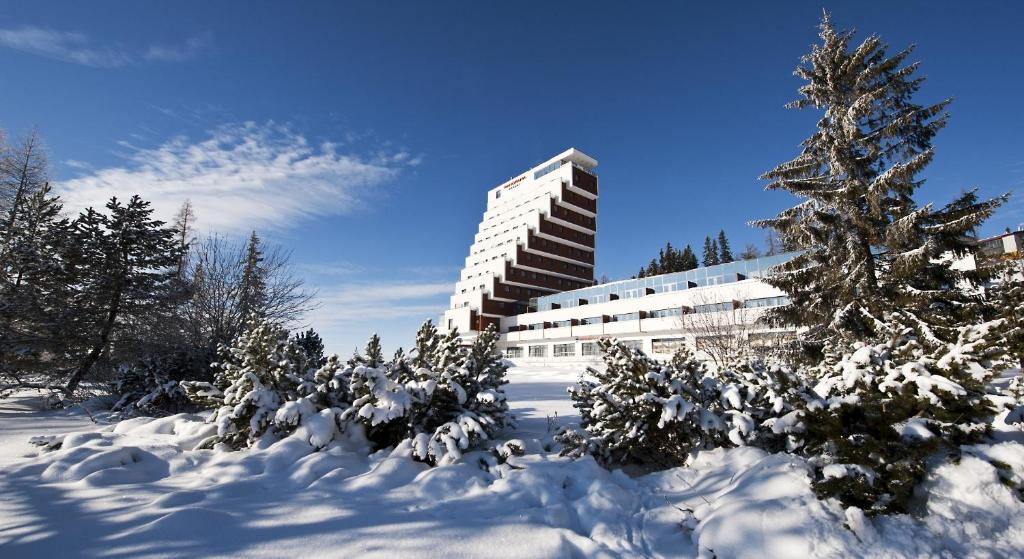 een sneeuwbedekte tuin met een gebouw en een boom bij Hotel Panorama Resort in Štrbské Pleso