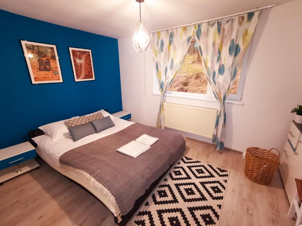 Cet appartement comprend une chambre dotée d'un lit avec un mur bleu et une fenêtre. dans l'établissement 105500 Apartment, à Buşteni