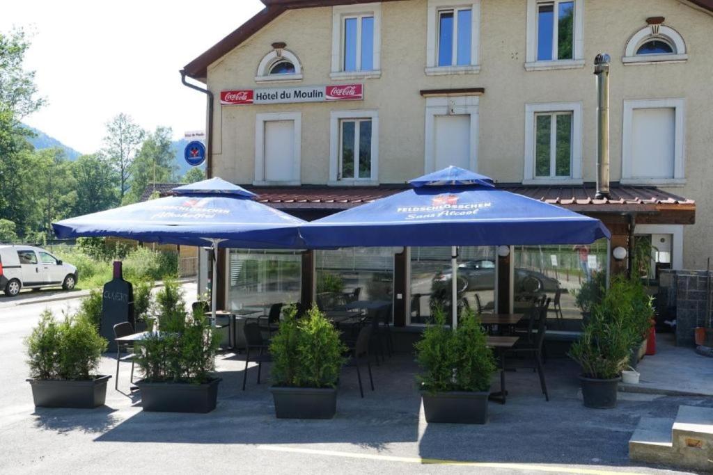 dois guarda-chuvas azuis sentados em frente a um edifício em Hotel Restaurant du Moulin em Fleurier