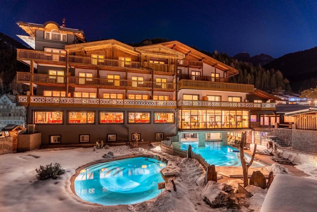 a large building with a swimming pool in the snow at Croce Bianca Leisure & Spa Hotel in Canazei