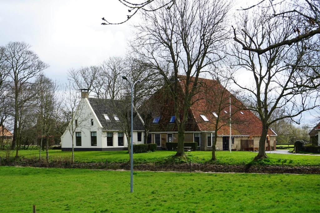 una casa bianca con alberi in un campo verde di B&B Piebengastate Welsrijp a Welsrijp