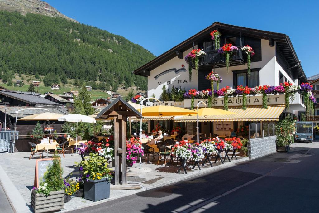 ein Gebäude mit Tischen, Stühlen und Blumen davor in der Unterkunft Hotel Mistral Superior in Saas-Fee